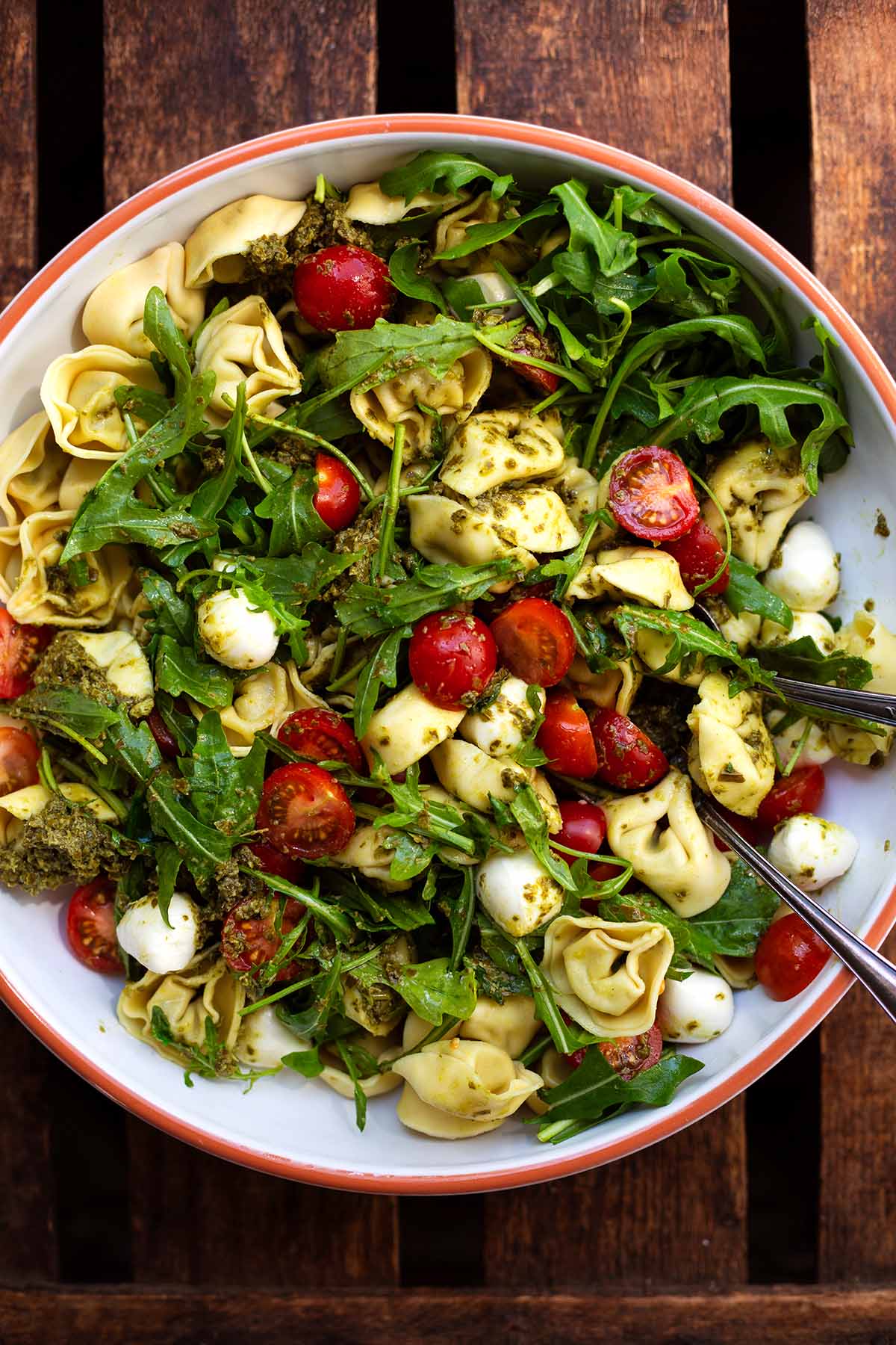 Fertiger Tortellinisalat mit Pesto in einer großen weißen Schüssel mit Besteck.