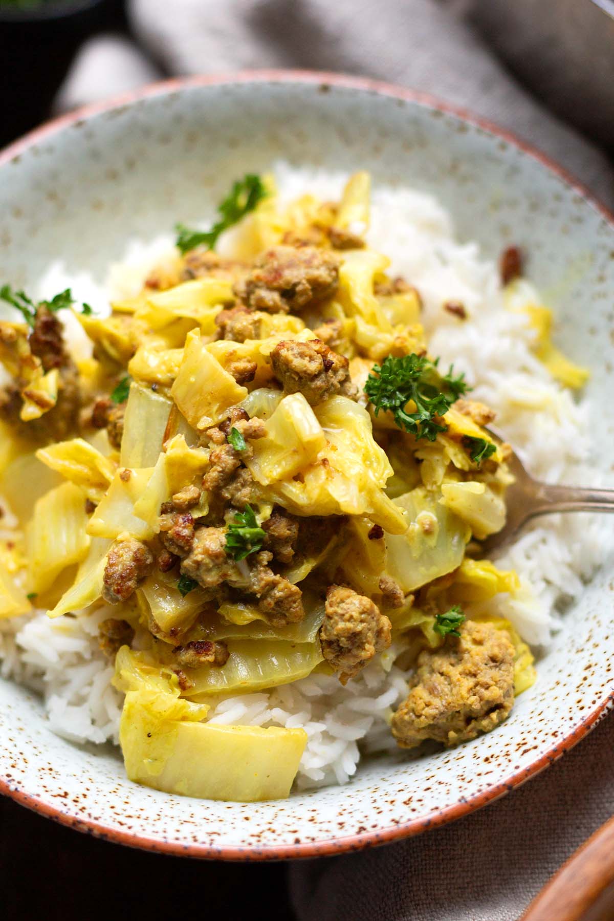 Fertige Chinakohl-Pfanne mit Hackfleisch. Angerichtet in einer grau-melierten Schüssel und garniert mit krauser Petersilie.