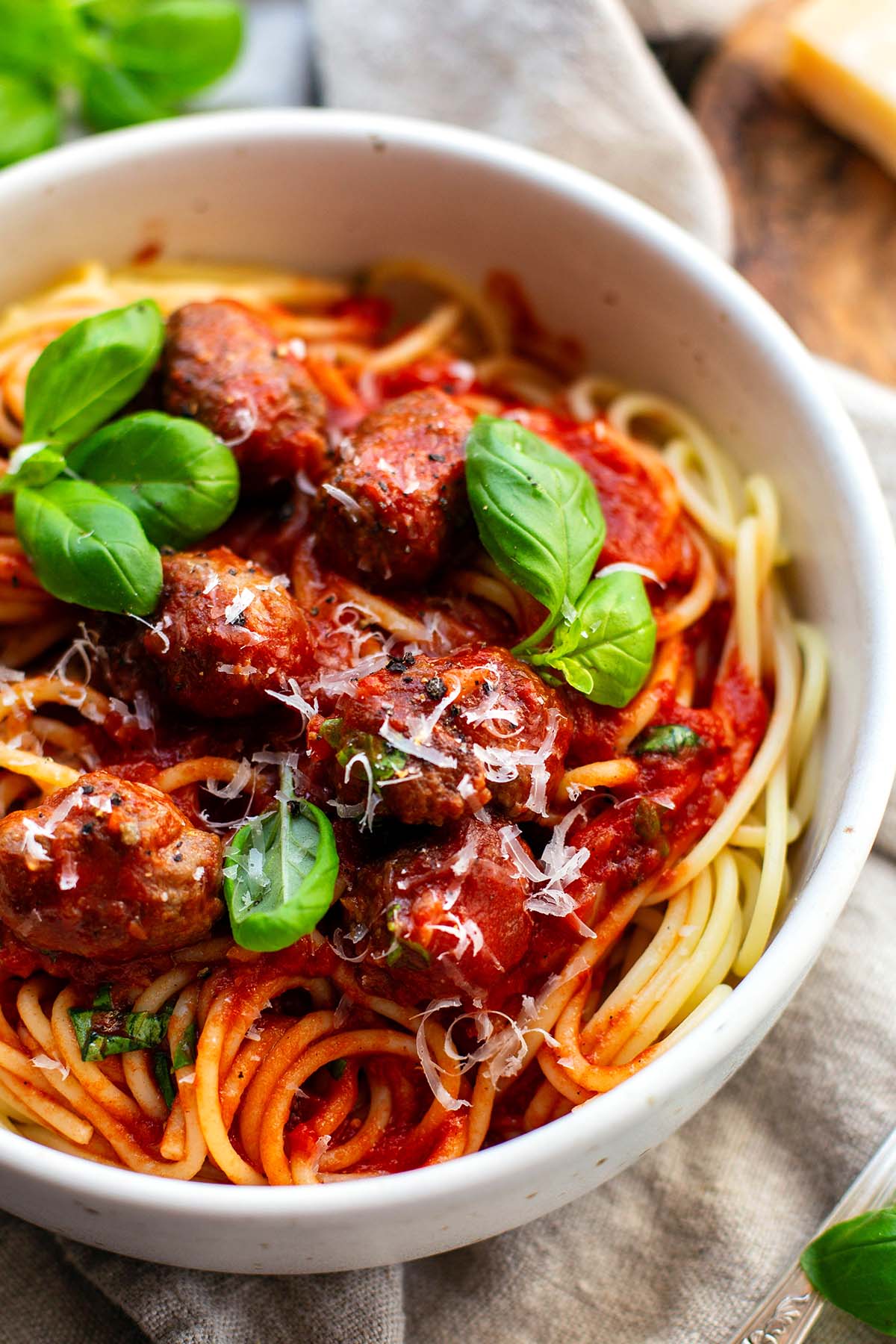 Fertige Spaghetti mit Fleischbällchen in einer weißen Schüssel. Garniert mit Basilikum und geriebenem Parmesan.