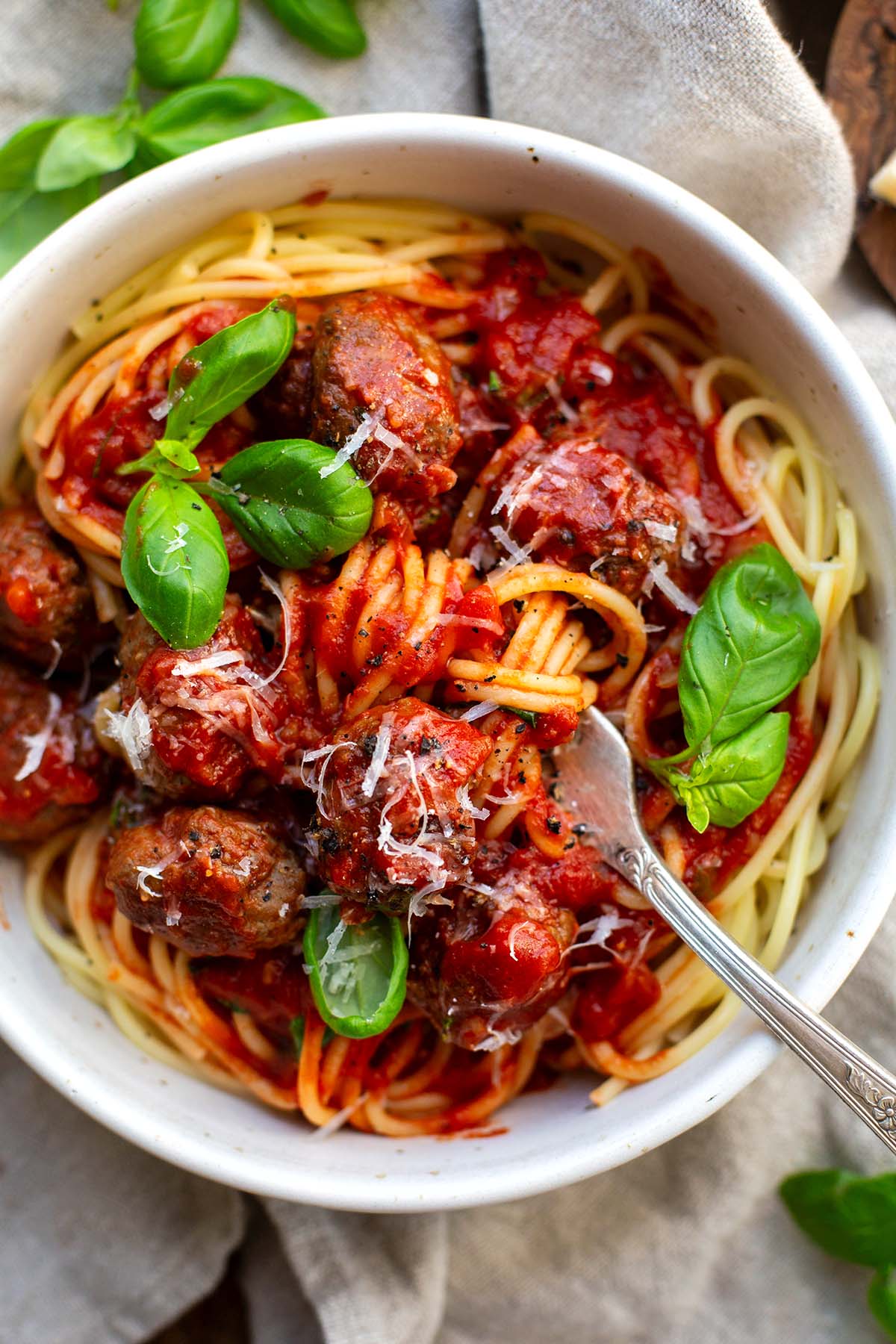 Fertige Spaghetti mit Fleischbällchen in einer weißen Schüssel. Garniert mit Basilikum und einer Gabel.