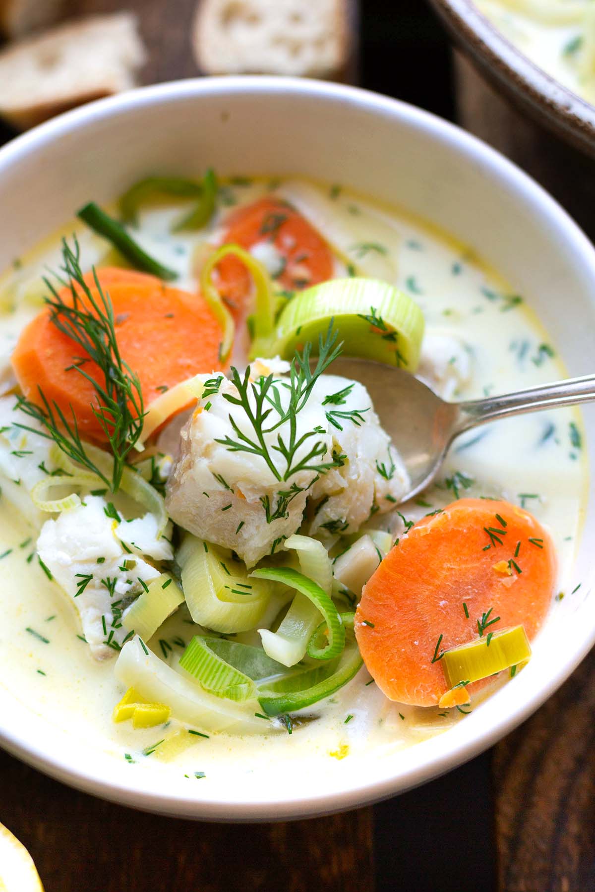 Fischsuppe mit Gemüse, Zitrone und Dill in einer weißen Schüssel auf dunklem Untergrund. 