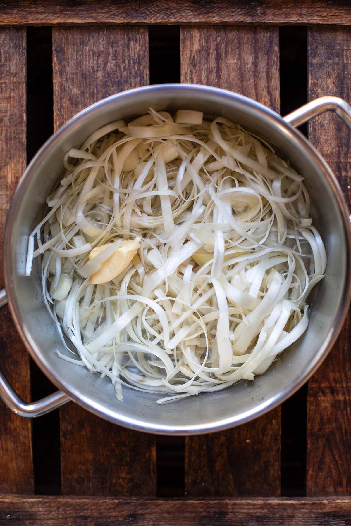 Spargelschalen und Butter in einem silbernen Topf auf dunklem Holzuntergrund.