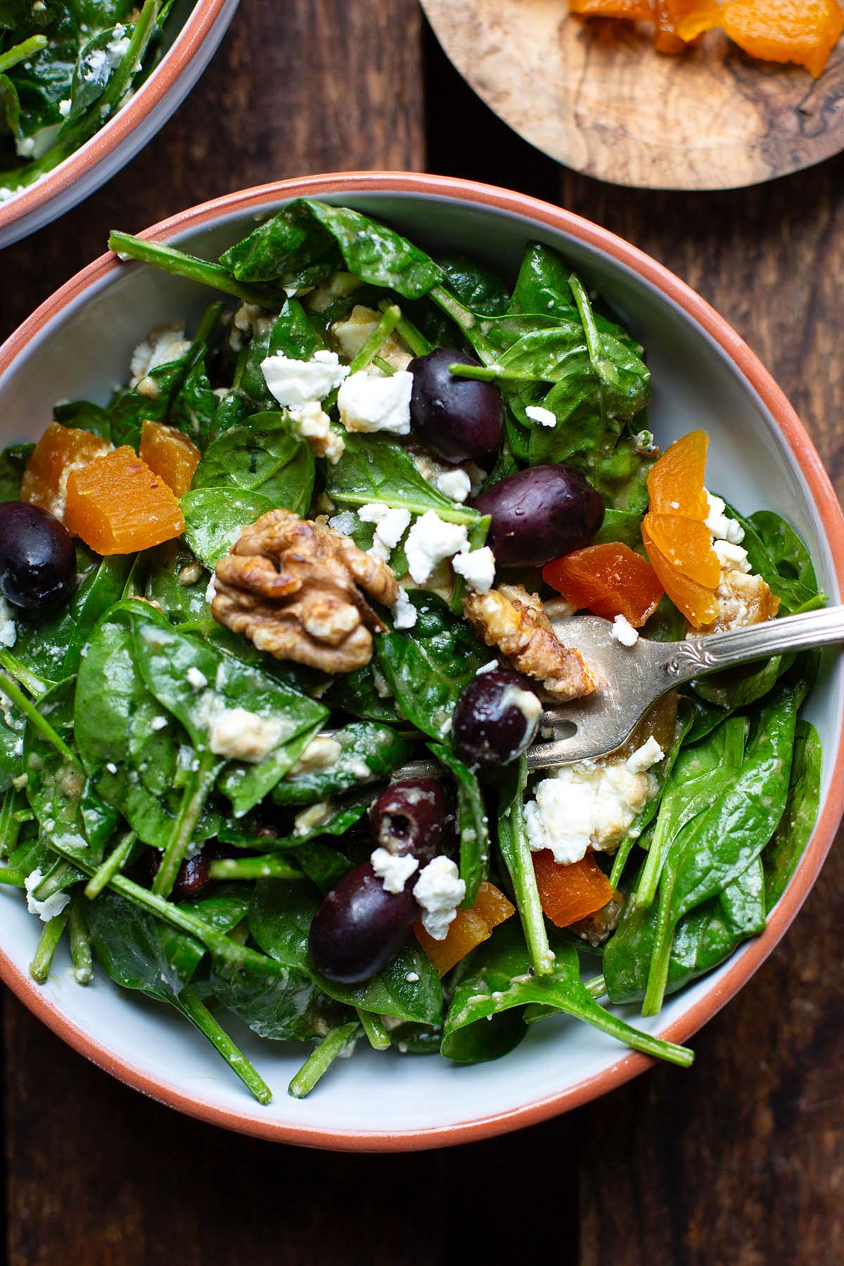 Fertiger Spinatsalat mit Feta und Honig-Senf-Dressing in einer weißen Schüssel auf dunklem Holzuntergrund. Eine silberne Gabel steckt im fertigen Salat.
