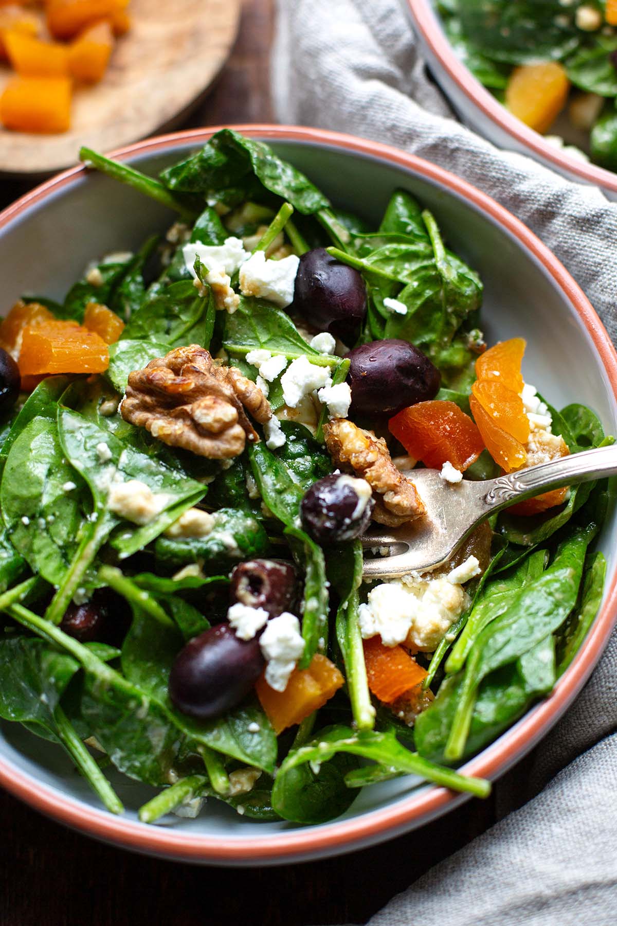 Fertiger Spinatsalat mit Feta und Honi-Senf-Dressing in weißer Schüssel mit orangem Rand. Silberne Gabel in der Schüssel mit Salat.