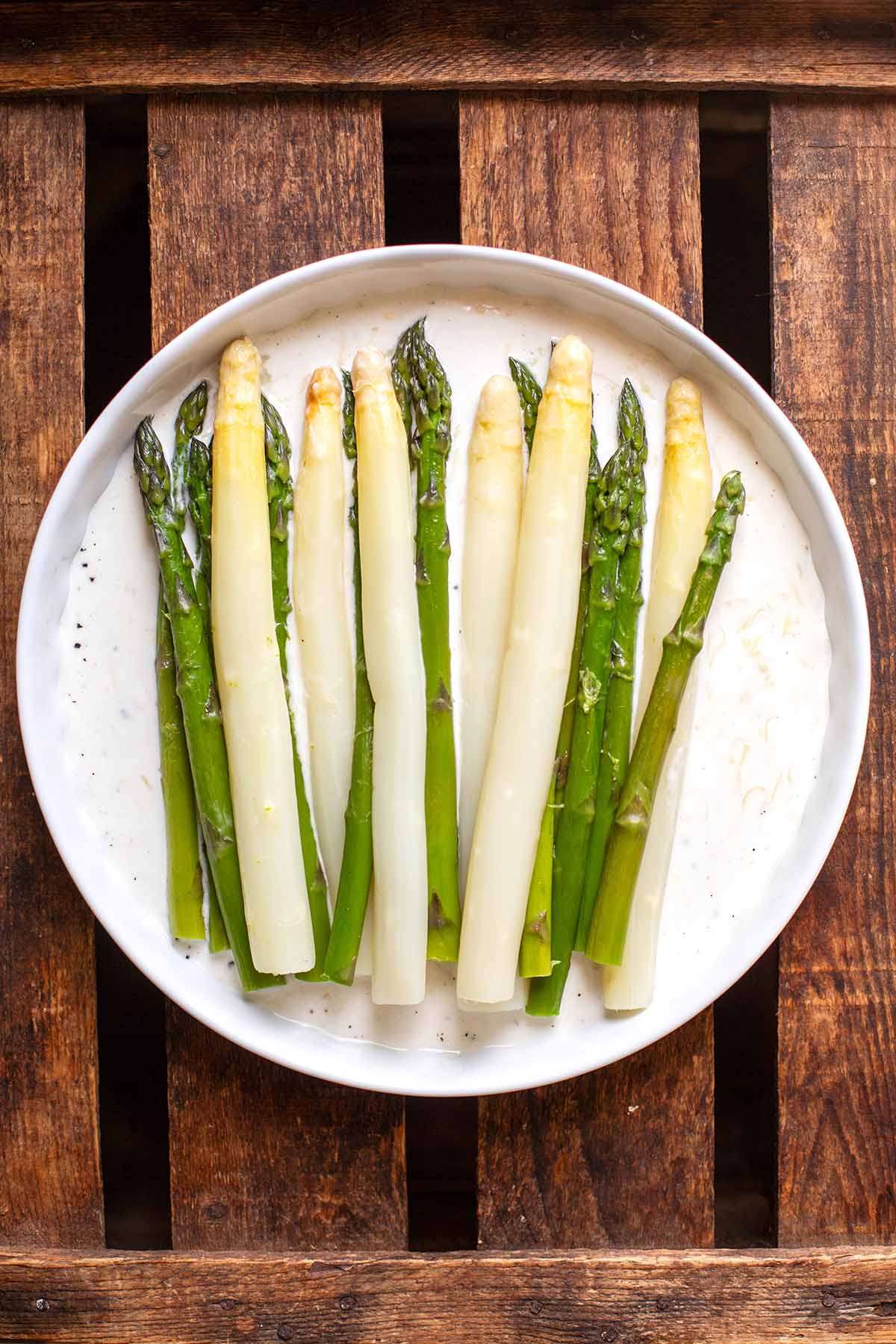 Grüner und weißer Spargel auf einem weißen Teller zusammen mit der Bèchamelsoße und geriebenem Käse.