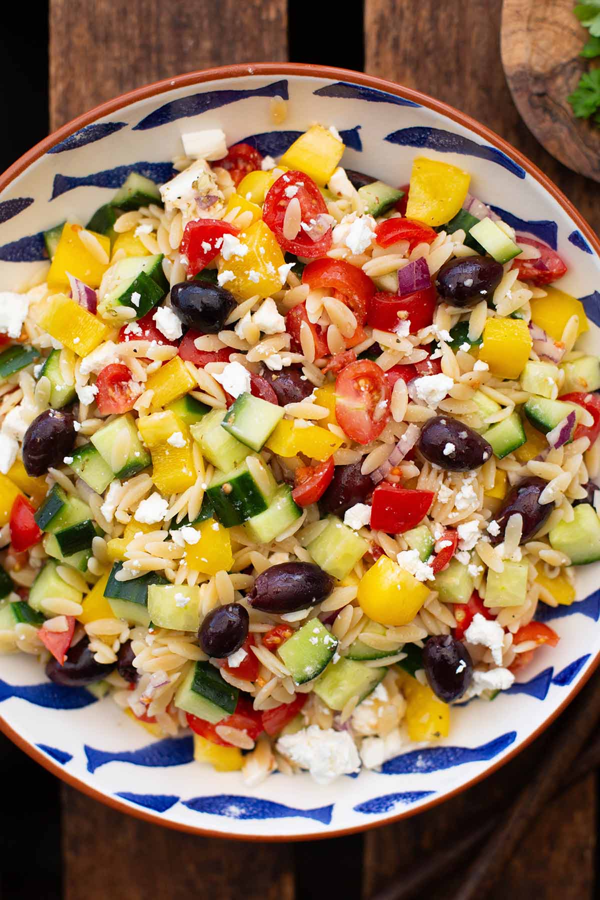 Fertiger griechischer Salat in einer weißen Schüssel mit braunem Rand und blauen Fischen. Die Schüssel steht auf einem dunklen Holzuntergrund.