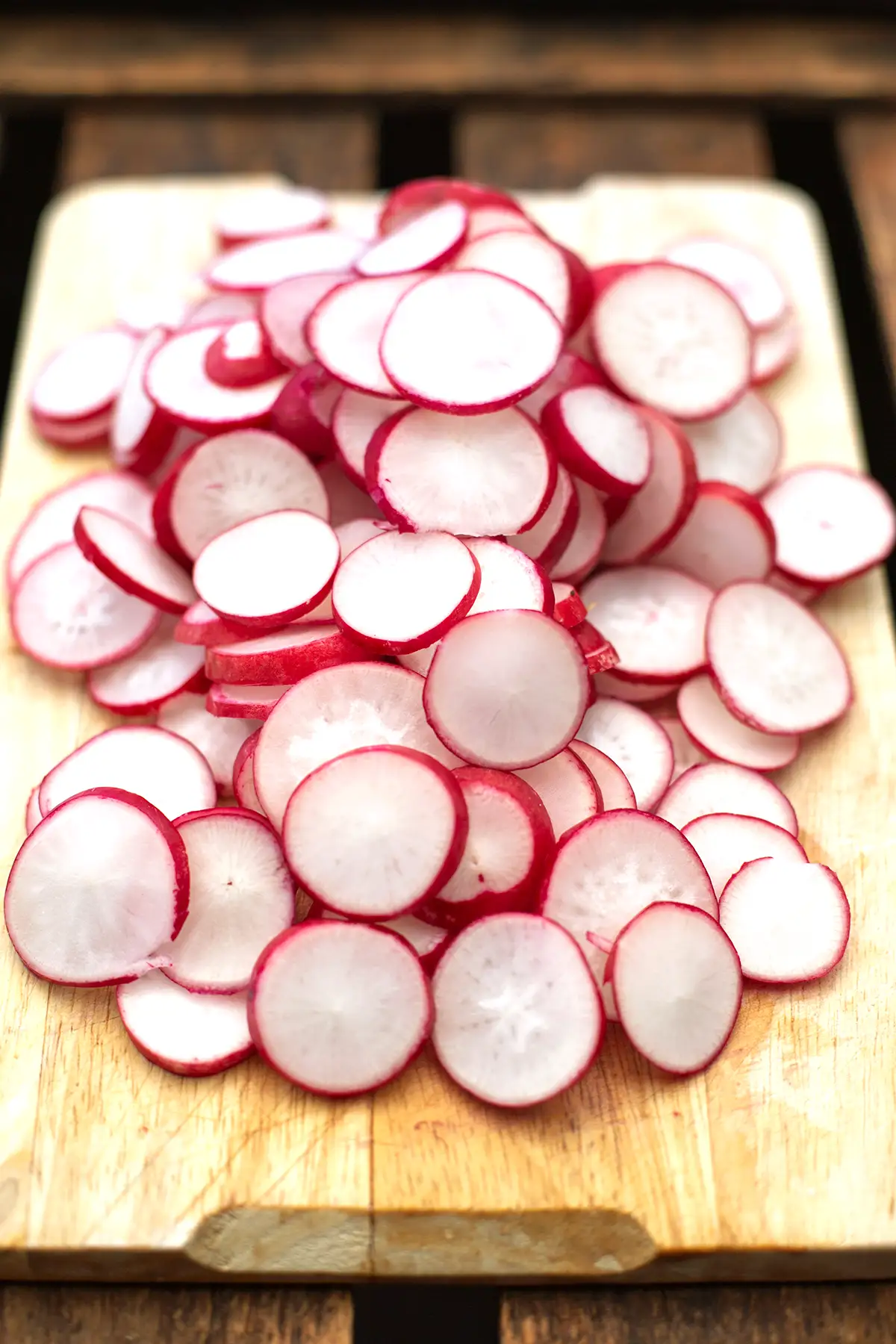 In Scheiben geschnittene Radieschen für den Radieschensalat nach Omas Rezept auf einem hellen Holzbrett. Das Holzbrett steht auf einem dunklen Holzuntergrund.