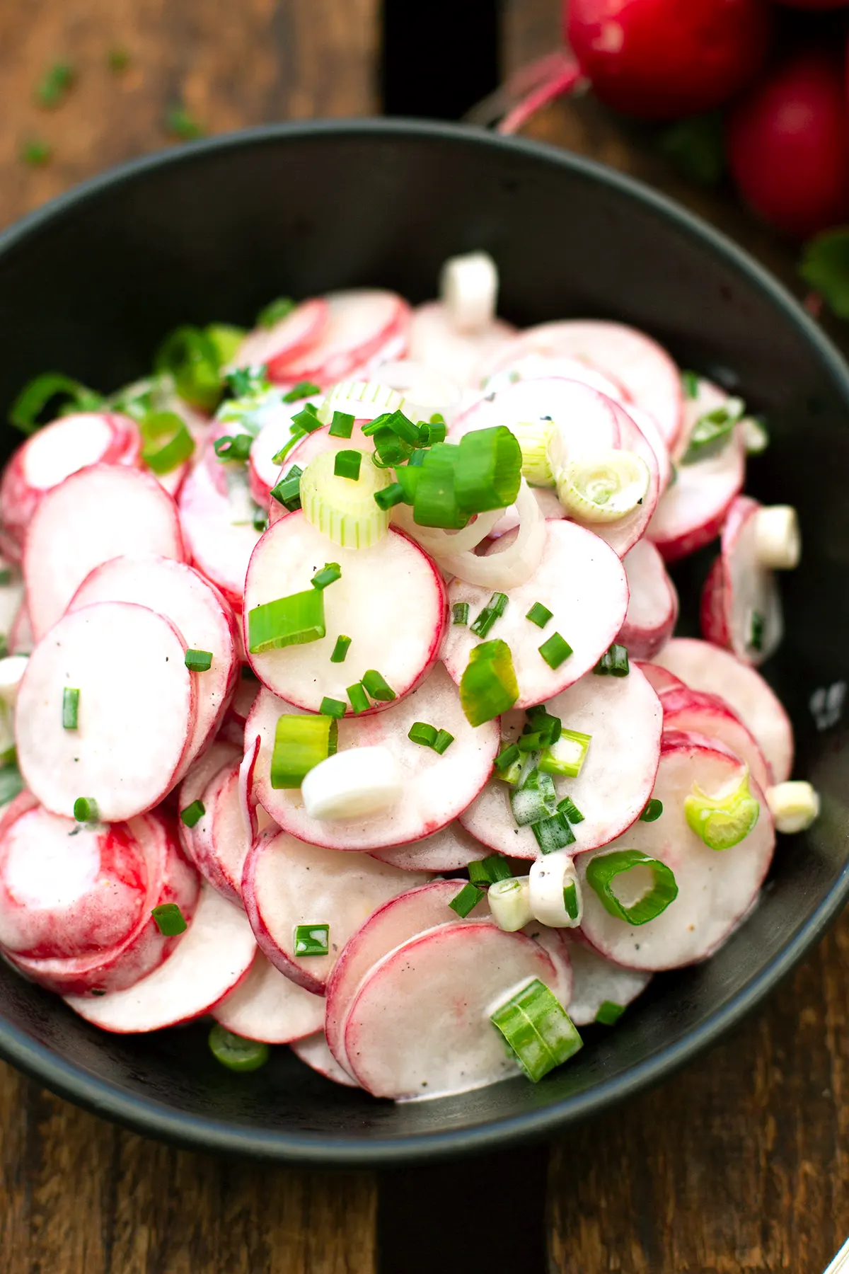 Radieschensalat einfaches Rezept mit Sahne wie von Oma - fertiger Salat in einer schwarzen Schüssel auf dunklem Holzuntergrund.