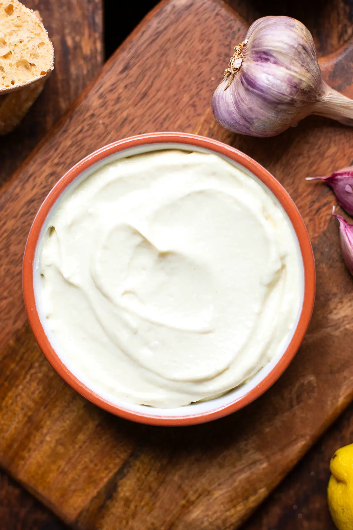 Fertige Aioli ohne Ei in einer weißen Schüssel mit orangem Rand auf einem Holzbrett.