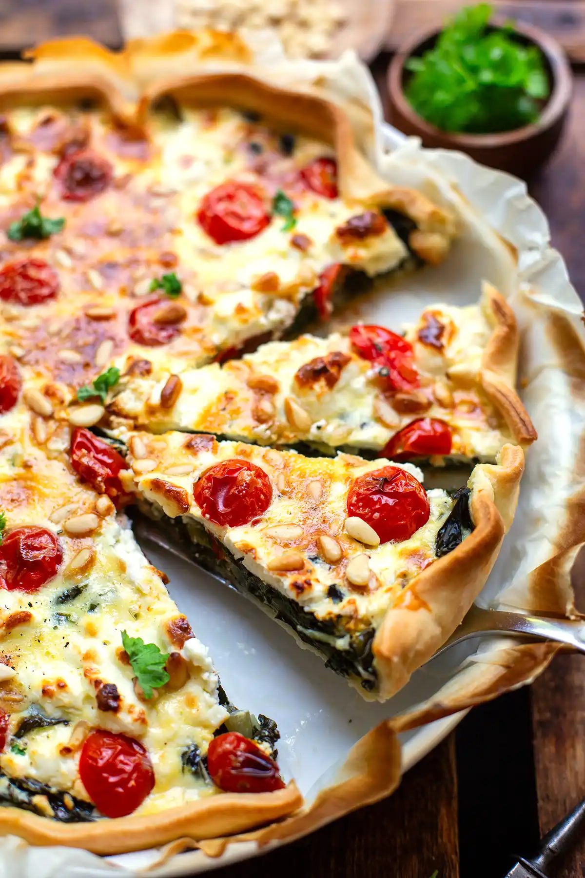 Die Fertige angeschnittene Mangold-Quiche in einer Quiche-Form. Zwei Stücke sind angeschnitten und eins davon wird mit einem Tortenheber angehoben - bereit zum Servieren.