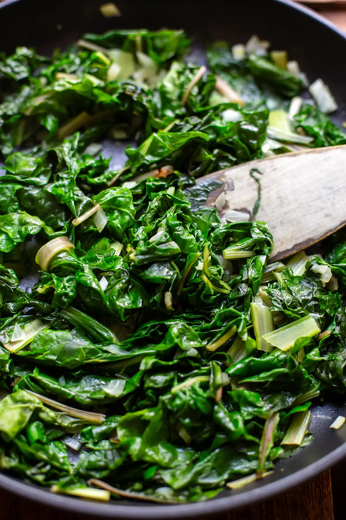 Klein geschnittener Mangold wird gerade in einer Pfanne angebraten. Zu sehen ist außerdem ein Pfannenwender aus Holz.
