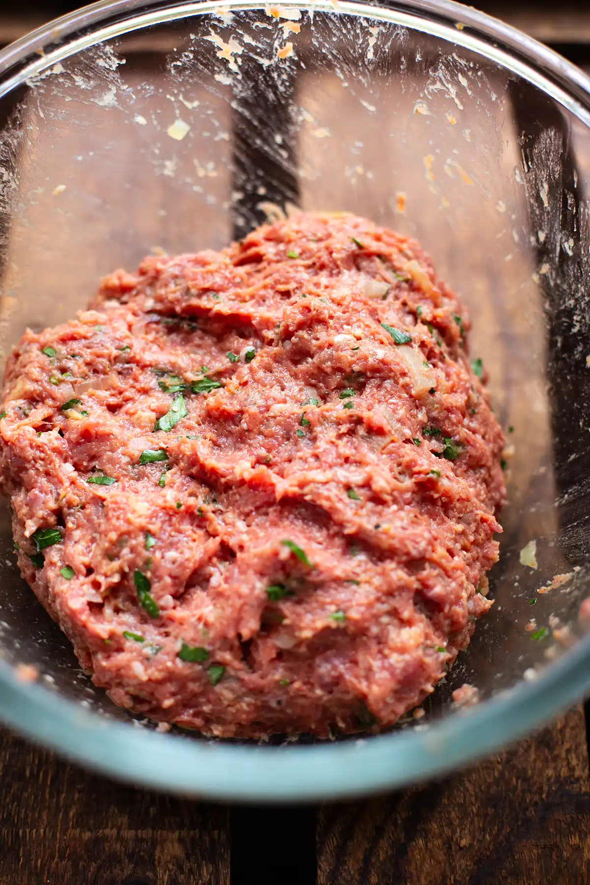 Frikadellen-Teig nach Omas Rezept vor dem Formen der Buletten in einer Glasschüssel auf dunklem Holzuntergrund.