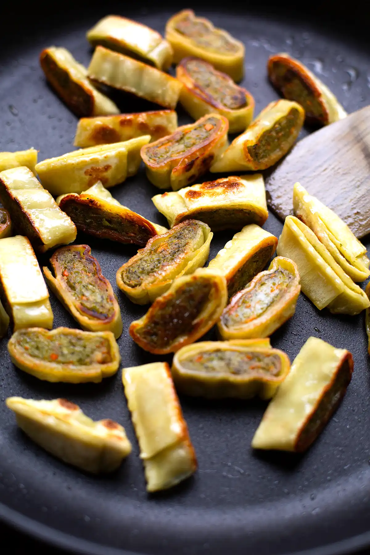 In Streifen geschnittene Maultaschen werden in einer schwarzen Pfanne knusprig angebraten und mit einem Holz-Pfannenwender gewendet. 