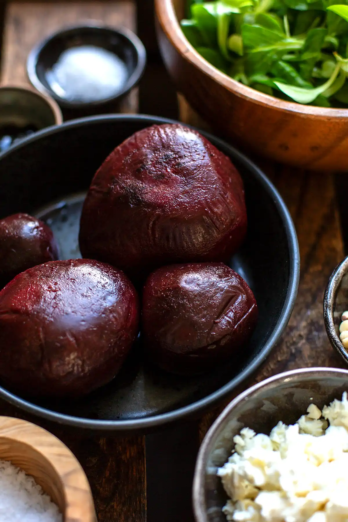Die Zutaten für das vegetarische Carpaccio in einzelnen Schüsseln. Zu sehen sind vakuumierte und ausgepackte rote Bete, Feldsalat, Salz, Balsamicocreme, Pinienkerne, Zucker und zerbröselter Feta.